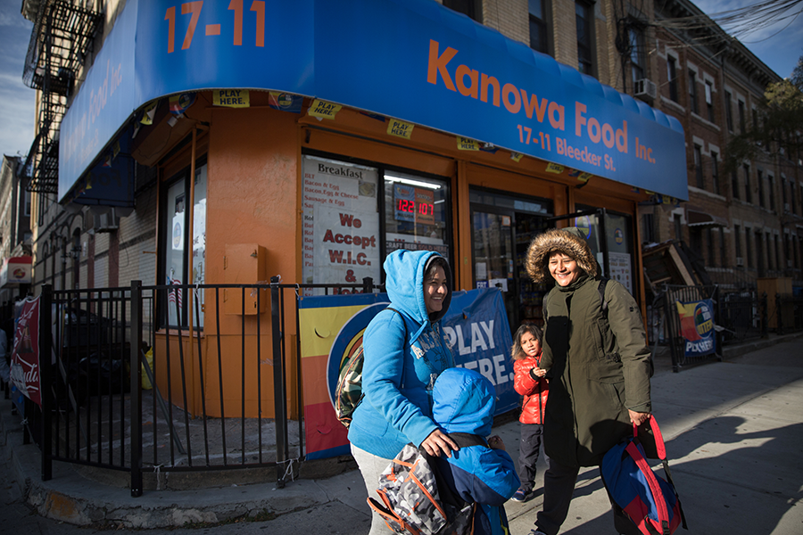 People on a sidewalk in front of a bodega