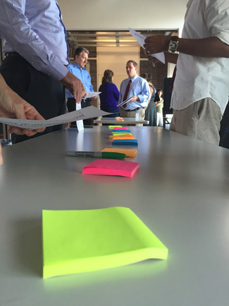 People stand around a long table; many brightly colored pads of sticky notes are on the table